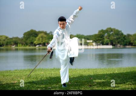 Jeune homme pratiquant le Tai Chi Sword traditionnel, Tai Ji dans le parc pour la santé, traditionnel chinois arts martiaux concept sur fond naturel . Banque D'Images