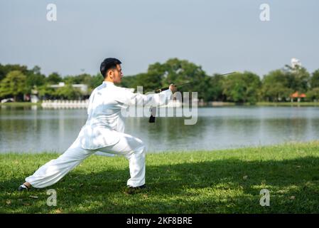 Jeune homme pratiquant le Tai Chi Sword traditionnel, Tai Ji dans le parc pour la santé, traditionnel chinois arts martiaux concept sur fond naturel . Banque D'Images