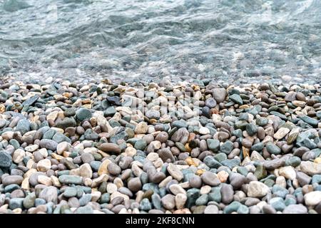 L'eau propre en cristal lave les cailloux qui se trouvent sur la plage de la mer. Les cailloux mouillés se trouvent près du bord de l'eau, attendant que les vagues se roulent de près Banque D'Images