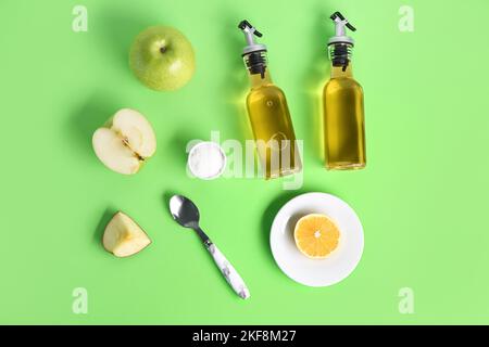 Composition avec bouteilles de vinaigre de cidre de pomme, fruits et sel sur fond vert Banque D'Images