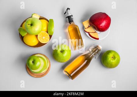 Composition avec bouteilles de vinaigre de cidre de pomme et fruits frais sur fond clair Banque D'Images