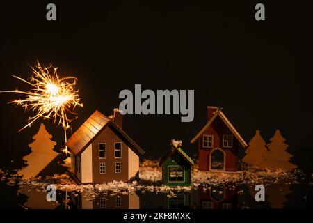 Composition avec feu de bois, décoration de Noël en bois, modèles de maison et neige sur fond sombre Banque D'Images