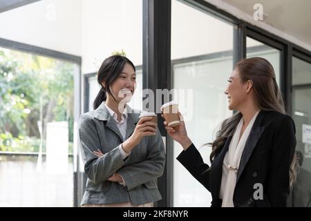 Divers employés discutant pendant la pause-café, marchant dans un bureau moderne, femme d'affaires asiatique portant des lunettes partageant des idées, discutant du projet avec Banque D'Images