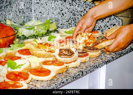 Assiette de laitue et de tomates sur le plan de travail, sur les hamburgers ouverts en rangée avec des frites, des steaks grillés hachés et de la sauce ketchup. Banque D'Images