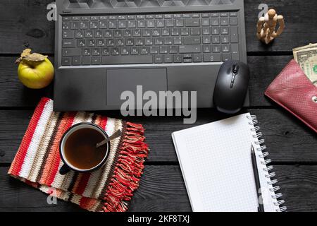 un bloc-notes noir pour ordinateur portable avec de l'argent pour le café se trouve sur la table de travail en bois noir, un ordinateur portable sur la table de travail pendant le travail, processus créatif, indépendant Banque D'Images