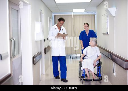 Vous allez vraiment bien. Une infirmière qui pousse une patiente en fauteuil roulant dans le couloir pendant qu'elle parle avec son médecin. Banque D'Images