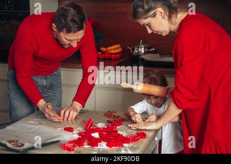 La veille de Noël, une soirée agréable pour les jeunes familles. Papa, maman et fils. Prépare des biscuits dans la cuisine. Atmosphère chaleureuse et accueillante. Vêtu de rouge. Banque D'Images