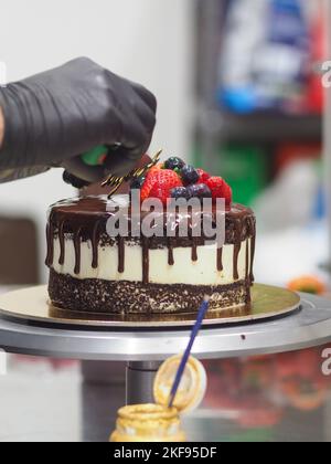 Chocolat noir gouttes gâteau d'anniversaire sucré, fruits frais framboise fraise bleuet canneberge sur le dessus, décoré avec de la peinture comestible dorée Banque D'Images