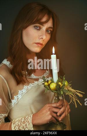 Belle femme de cheveux rouges avec bougie. Portrait en lumière douce et chaude Banque D'Images