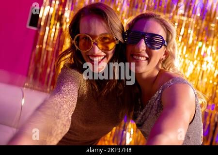 Portrait de deux amies caucasiennes souriantes dans des lunettes de soleil embrassant dans une boîte de nuit Banque D'Images