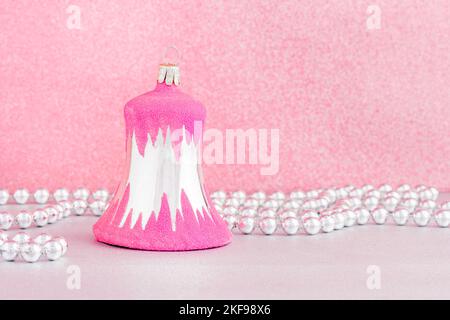 Une boule de noël rose vintage en forme de cloche avec une guirlande argentée ornée de perles sur fond rose. Banque D'Images