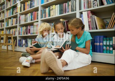 Groupe d'enfants lisant en s'asseyant sur le sol dans la bibliothèque Banque D'Images