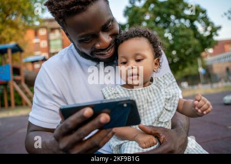 Jolie petite fille regardant quelque chose sur son père téléphone mobile Banque D'Images