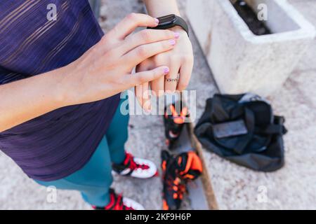 Photo horizontale d'une jeune fille méconnaissable se prépare sur sa montre intelligente pour sortir sur des patins en ligne Banque D'Images