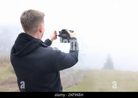 Jeune photographe masculin dans un pré brumeux prenant des photos. Banque D'Images