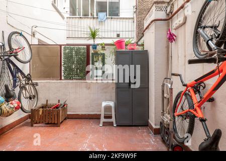 Patio intérieur d'une maison avec des vélos suspendus, des meubles de terrasse et des sols en argile brune Banque D'Images