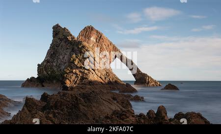 Bow Fiddle Rock dans les Highlands écossais. Forme d'arc sculptée dans la face rocheuse. Obturateur lent pour créer une eau douce qui se balade sur la plage de galets. Être Banque D'Images