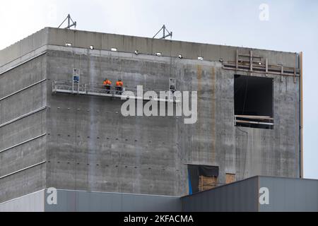 Deux ouvriers du bâtiment portant un harnais de sécurité et des ceintures de sécurité travaillant sur un grand bâtiment se tiennent sur une plate-forme suspendue à un palan Banque D'Images