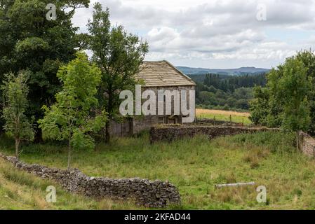 Ancienne grange en pierre abandonnée et maison à la campagne. Toit en pierre avec herbe verte et arbres environnants. Collines et nuages en arrière-plan Banque D'Images