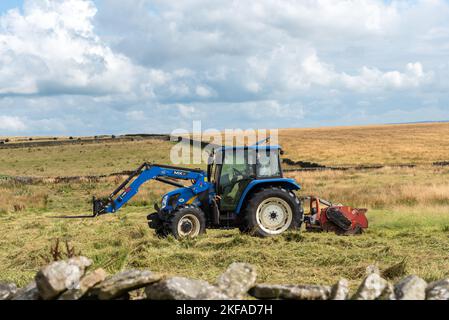 Prise le 31 août 2022, Slaidburn, Clitheroe, Lancashire, Royaume-Uni. Agriculteur coupant son champ d'herbe dans son tracteur bleu. Champs verts et ciel bleu ensoleillé. Banque D'Images