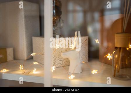 Derrière le verre d'une armoire avec vaisselle, les étagères sont décorées de jouets de Noël, guirlandes lumineuses, cadeaux dans un emballage rose. Jouets en forme de Banque D'Images