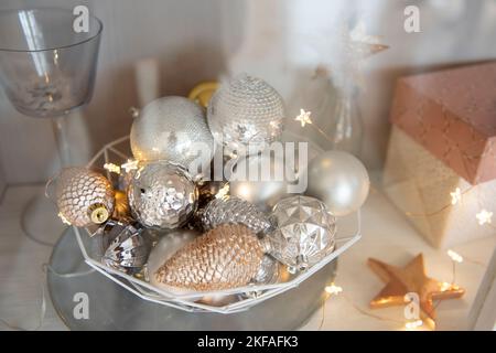 Derrière le verre d'une armoire avec vaisselle, les étagères sont décorées de jouets de Noël, guirlandes lumineuses, cadeaux dans un emballage rose. Jouets en forme de Banque D'Images