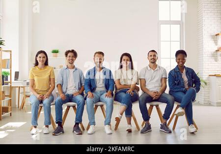 Portrait de jeunes multiraciaux souriants dans des vêtements décontractés assis dans la rangée sur des chaises. Banque D'Images