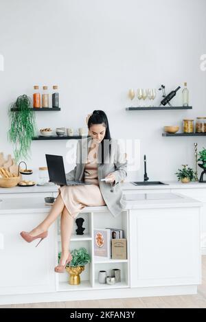 Une jeune fille travaille de la maison. La femme dans la cuisine travaille à son ordinateur portable pour payer les factures. Le stress de la vie quotidienne. La femme a la santé interne Banque D'Images