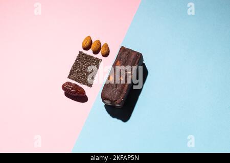 Barres de bonbons aux fruits à la date des protéines fitness avec noix et amandes de fruits et graines de pavot de chia vue de dessus sur fond bleu rose avec espace pour copier et place pour Banque D'Images