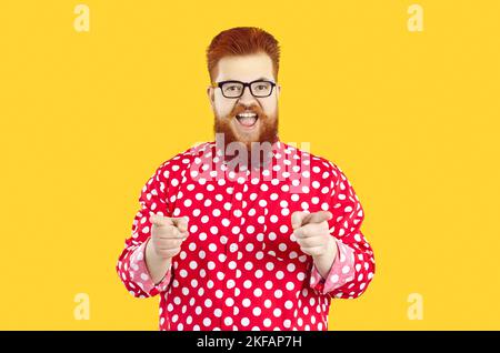 Drôle heureux gras barbu homme dans la chemise à pois et les lunettes souriant et pointant vers l'appareil photo Banque D'Images