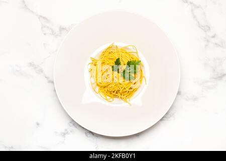 Spaghetti aux feuilles de persil dans une assiette blanche sur un comptoir de cuisine en marbre Banque D'Images
