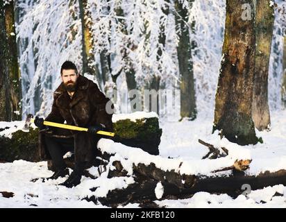 Homme en fourrure tient la hache jaune. Macho avec barbe Banque D'Images