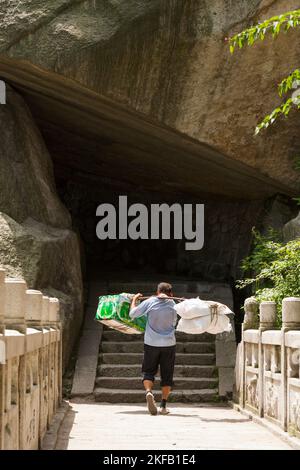 Homme travaillant à Huashan Mountain / Mont Hua / Mont Hua près de Huayin, Weinan, Chine. Il porte / porte une lourde charge de fournitures vers le haut de la voie / piste à l'aide d'un bâton de transport. (125) Banque D'Images