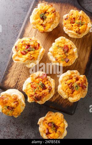 des muffins savoureux de pâte feuilletée avec œufs, jambon et cheddar sur une planche en bois sur la table. Vue verticale du dessus Banque D'Images