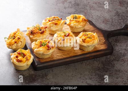 Mini-tasses croustillantes de pâte feuilletée farcies aux œufs, au fromage et au jambon sur une planche de bois sur la table. Horizontale Banque D'Images