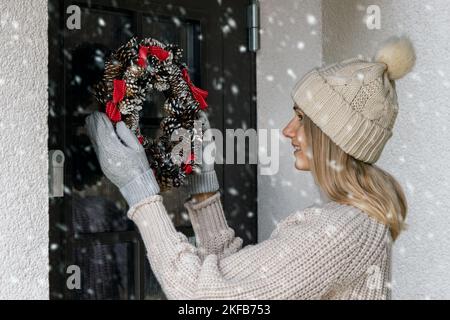 une femme est accrochée à une couronne de l'avent de noël sur une porte d'entrée de la maison. décoration de la maison Banque D'Images