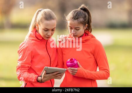 Une jeune entraîneuse et une jeune femme vérifient ses performances sportives sur une tablette. Banque D'Images