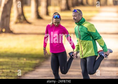 Deux athlètes amateurs mature homme et jeune femme se réchauffent avant de courir, faisant le corps inférieur s'étirant dans le parc. Banque D'Images