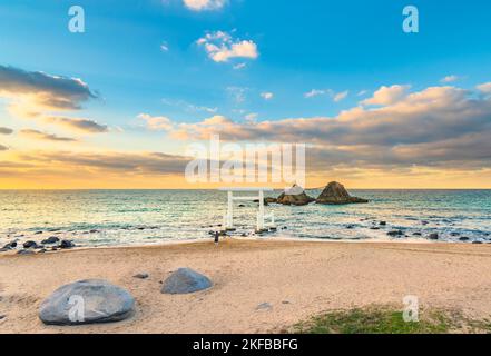 Une personne priant sur la plage d'Itoshima de Fukuoka debout devant une porte Shinto torii blanche menant à la célèbre Sakurai Futamigaura's Meoto I Banque D'Images