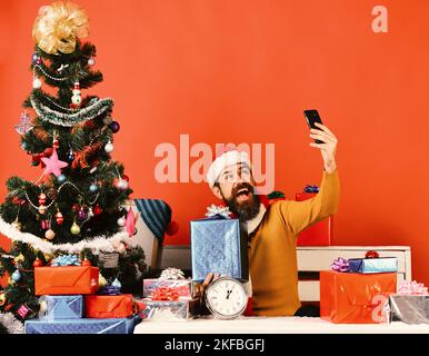 Le père Noël tient le téléphone cellulaire et la boîte à cadeaux. Homme avec barbe Banque D'Images