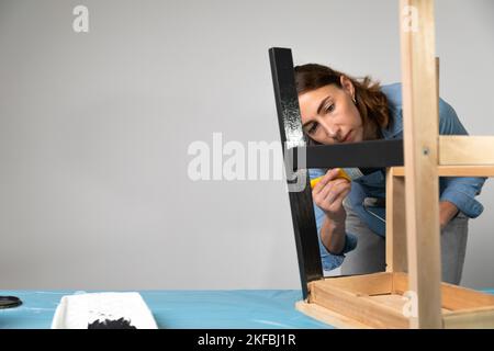 Les jeunes femmes se préparant à restaurer un escabeau pour les enfants comme une amélioration de maison de passe-temps. Sur une table couverte. Peindre avec un pinceau Banque D'Images