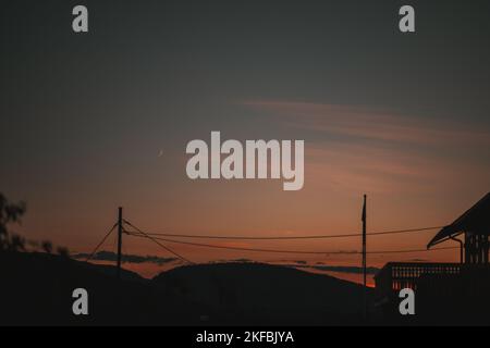 Une vue vague de la demi-lune dans le ciel au coucher du soleil, sous les silhouettes des pôles de pouvoir et une maison Banque D'Images