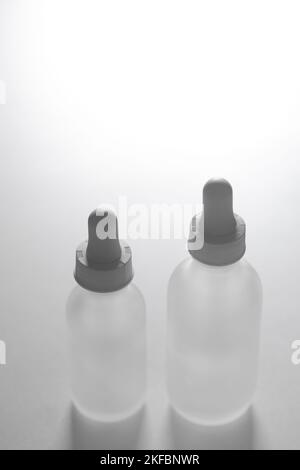 Gros plan de deux flacons compte-gouttes en verre translucide vides. Flacons de différentes tailles sur fond blanc. Espace de copie et de maquette vertical de style de vie de beauté. Banque D'Images
