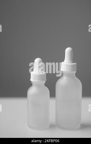 Gros plan de deux flacons compte-gouttes en verre translucide vides. Flacons de différentes tailles sur fond blanc bicolore. Maquette verticale et espace de copie. Banque D'Images