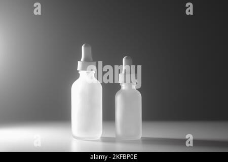 Deux flacons compte-gouttes en verre translucide vides sur fond blanc bicolore. Flacons de différentes tailles au centre. Éclairage latéral spectaculaire. Espace de copie de beauté. Banque D'Images
