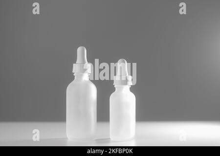 Deux flacons compte-gouttes en verre translucide vides sur fond blanc bicolore. Flacons de différentes tailles placés au centre. Éclairage latéral brillant. Espace de copie de beauté. Banque D'Images