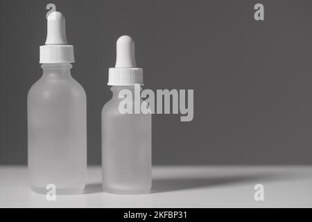 Gros plan de deux flacons compte-gouttes en verre translucide vides. Flacons de différentes tailles sur fond blanc bicolore. Maquette horizontale et espace de copie. Banque D'Images