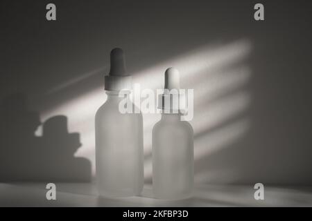 Deux flacons compte-gouttes en verre translucide vides. Flacons de différentes tailles sur fond blanc avec lumière naturelle et appliquée. Espace de copie horizontal. Banque D'Images