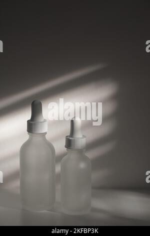 Deux flacons compte-gouttes en verre translucide vides. Flacons de différentes tailles sur fond blanc avec lumière naturelle et appliquée. Espace de copie de beauté vertical. Banque D'Images
