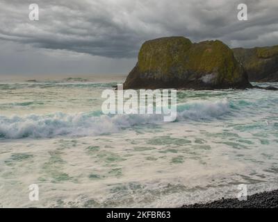 Océan qui fait rage, vagues de mousse blanche qui se brisent sur le rivage. Au loin, vous pouvez voir un rocher recouvert de mousse verte. Des nuages orageux dans le ciel. Élément, Banque D'Images